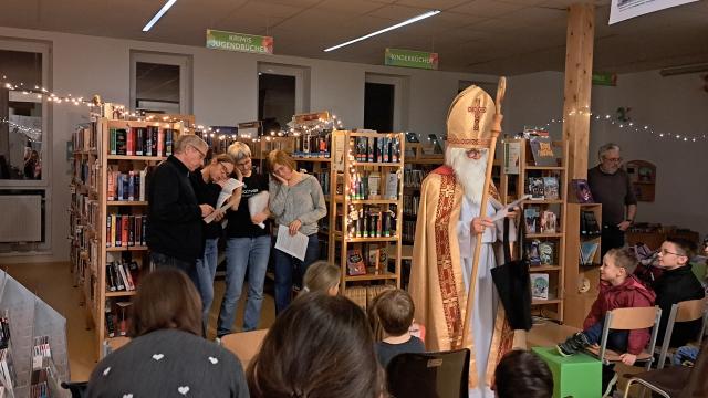 Nikolaus und Mitglieder des Bibliotheksteams "spielen" die Legende von Nikolaus und den drei armen Töchtern: Familie schläft während Nikolaus sie beschenkt